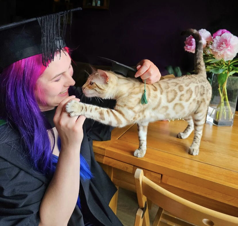 graduation cat affectionately pawing a woman in a graduation gown.
